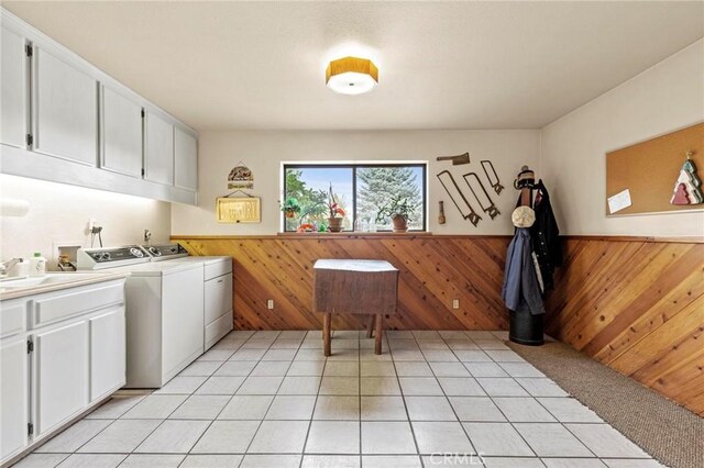 laundry area with sink, washing machine and dryer, cabinets, light tile patterned flooring, and wood walls