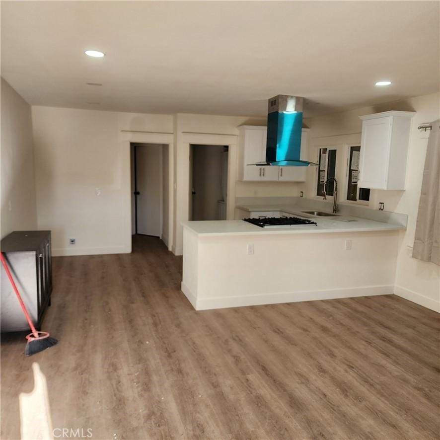 kitchen with sink, white cabinetry, extractor fan, wood-type flooring, and kitchen peninsula