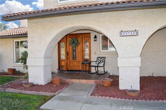 view of exterior entry with a porch, stucco siding, and a tile roof