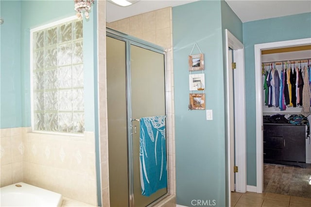 bathroom with a walk in closet, tile patterned flooring, a stall shower, and a garden tub
