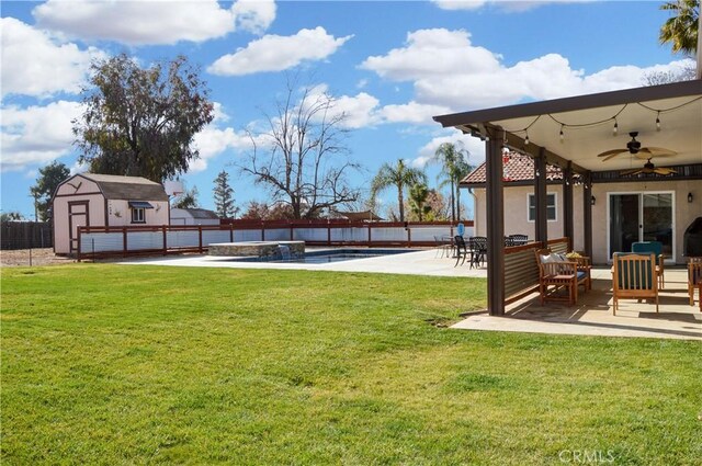 view of yard with fence, a storage shed, an outbuilding, a ceiling fan, and a patio