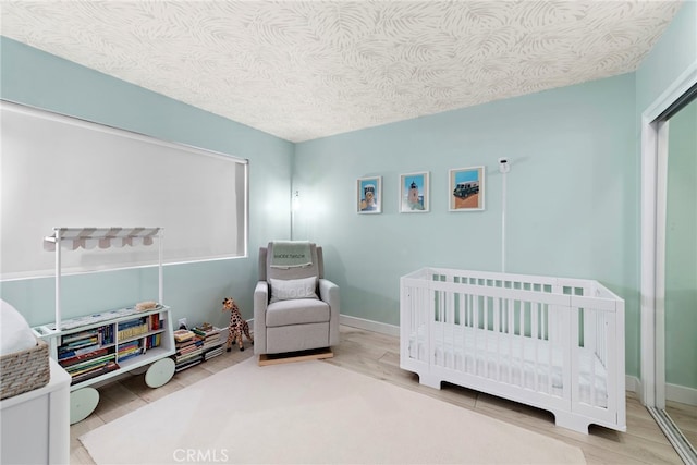 bedroom featuring a crib, wood-type flooring, and a textured ceiling