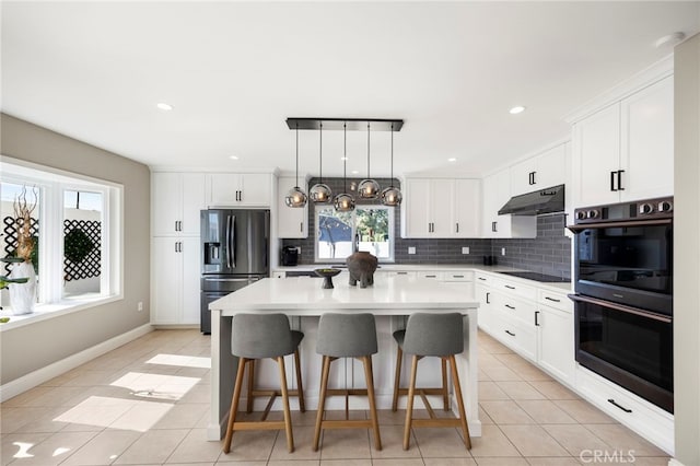 kitchen featuring black appliances, under cabinet range hood, a kitchen bar, and decorative backsplash