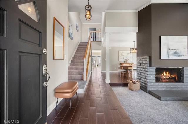 entryway with crown molding, wood tiled floor, a lit fireplace, baseboards, and stairs