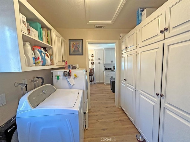 laundry area featuring washer and dryer, light hardwood / wood-style floors, and cabinets