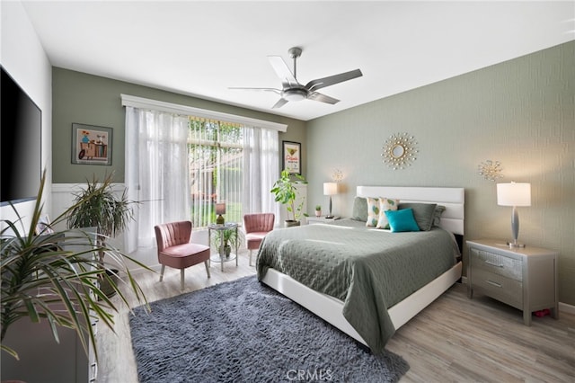 bedroom with an accent wall, light wood-type flooring, and a ceiling fan