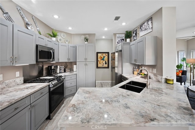 kitchen with stainless steel appliances, visible vents, gray cabinetry, a sink, and a peninsula