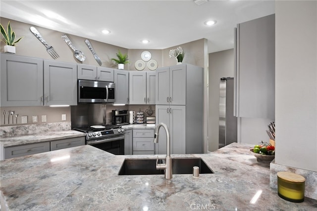 kitchen featuring appliances with stainless steel finishes, a peninsula, light stone countertops, gray cabinets, and a sink