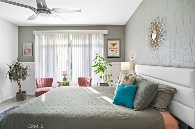 bedroom with wallpapered walls, baseboards, a ceiling fan, an accent wall, and wood finished floors