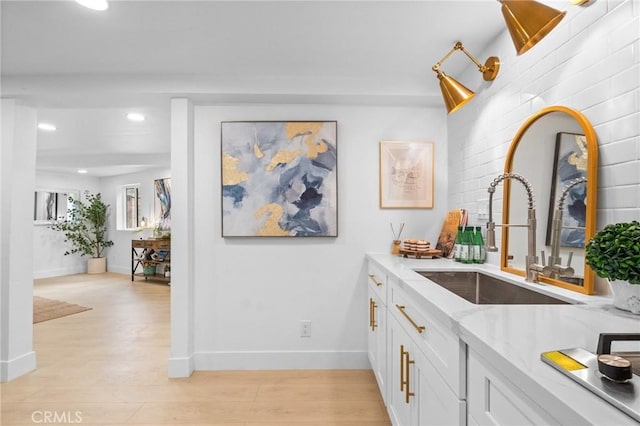 bar featuring white cabinetry, sink, light hardwood / wood-style flooring, and light stone countertops