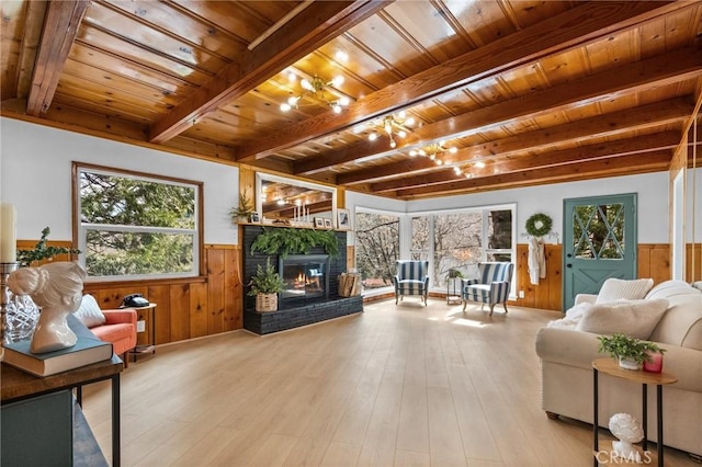 living room featuring wood ceiling, light hardwood / wood-style floors, a brick fireplace, and beamed ceiling