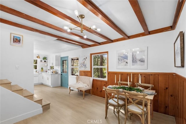 interior space with a chandelier, wood walls, beamed ceiling, and light wood-type flooring