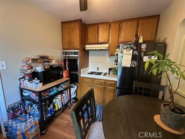 kitchen with backsplash, tile countertops, hardwood / wood-style flooring, and black appliances