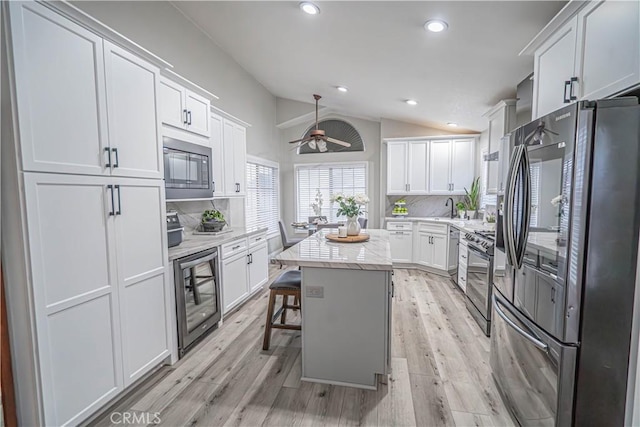 kitchen with appliances with stainless steel finishes, white cabinetry, a kitchen breakfast bar, wine cooler, and a kitchen island