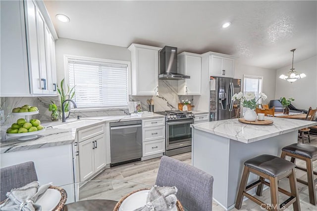 kitchen with wall chimney range hood, sink, hanging light fixtures, stainless steel appliances, and a center island