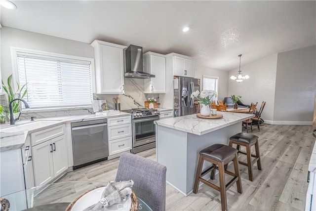 kitchen with a center island, appliances with stainless steel finishes, pendant lighting, wall chimney range hood, and white cabinets