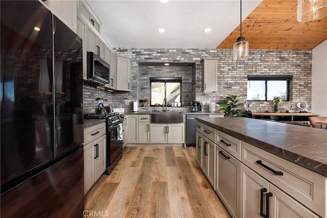 kitchen featuring backsplash, black appliances, decorative light fixtures, light wood finished floors, and a sink