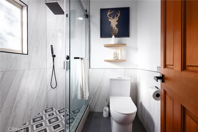 bathroom featuring tile patterned flooring, a wainscoted wall, toilet, tile walls, and a stall shower