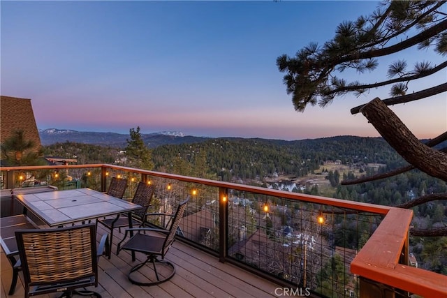 deck at dusk with outdoor dining area and a mountain view