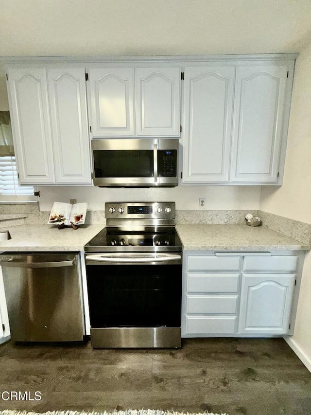 kitchen featuring dark wood-type flooring, appliances with stainless steel finishes, light stone counters, and white cabinets