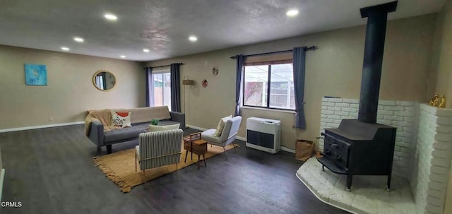 living room with heating unit, baseboards, wood finished floors, and a wood stove