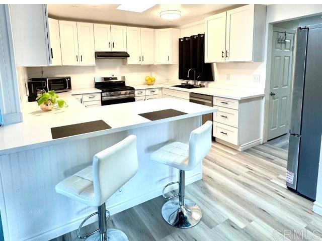 kitchen featuring appliances with stainless steel finishes, a breakfast bar, white cabinetry, sink, and kitchen peninsula