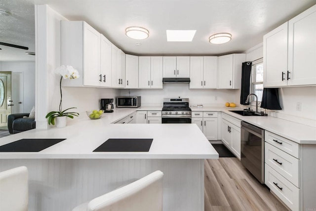 kitchen with white cabinets, appliances with stainless steel finishes, a peninsula, light countertops, and a sink