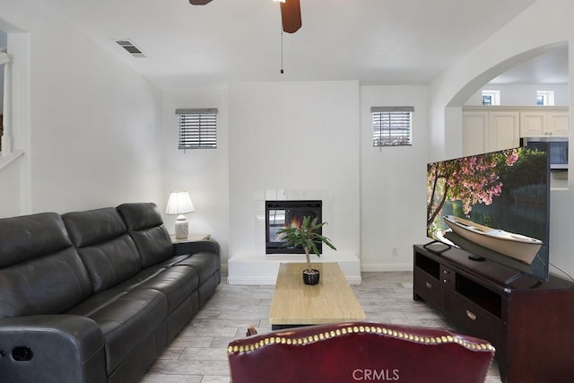 living room featuring a ceiling fan, a glass covered fireplace, visible vents, and wood tiled floor