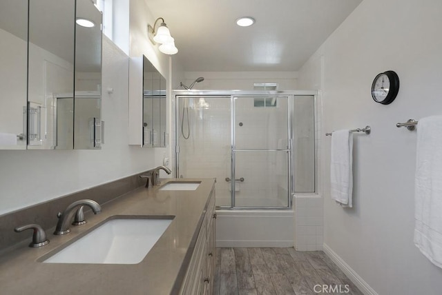 full bathroom featuring shower / bath combination with glass door, baseboards, a sink, and wood finished floors