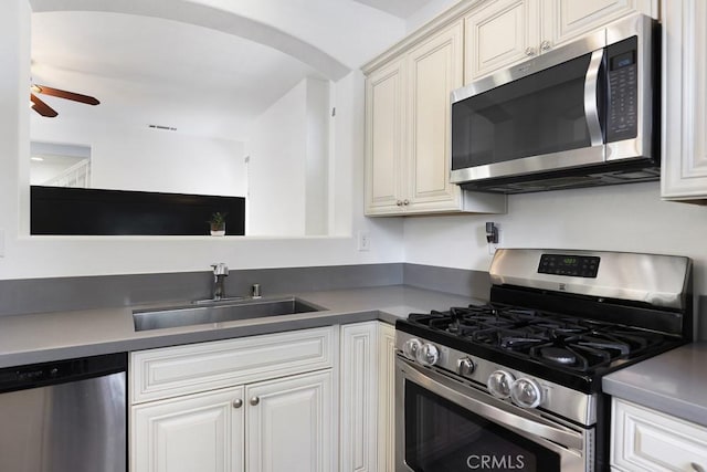 kitchen featuring arched walkways, a ceiling fan, dark countertops, appliances with stainless steel finishes, and a sink