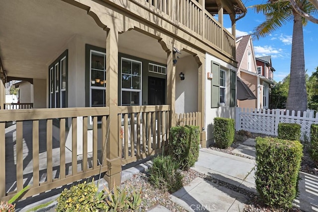 property entrance featuring fence, a balcony, and stucco siding