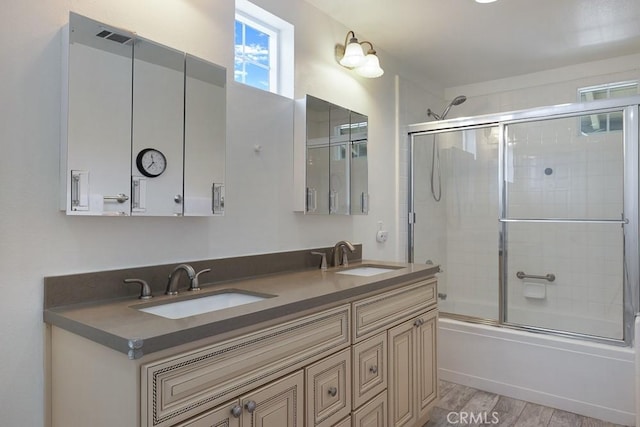 bathroom with double vanity, combined bath / shower with glass door, a sink, and wood finished floors