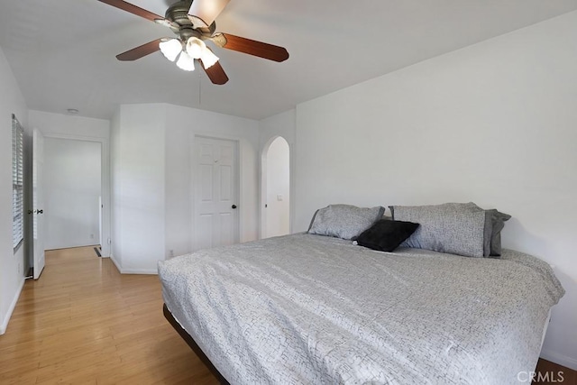 bedroom featuring light wood-style floors, arched walkways, and ceiling fan