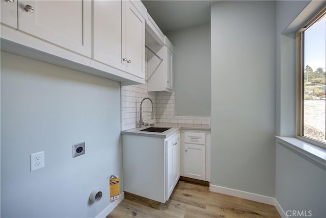 laundry area with electric dryer hookup, a wealth of natural light, light hardwood / wood-style floors, and cabinets