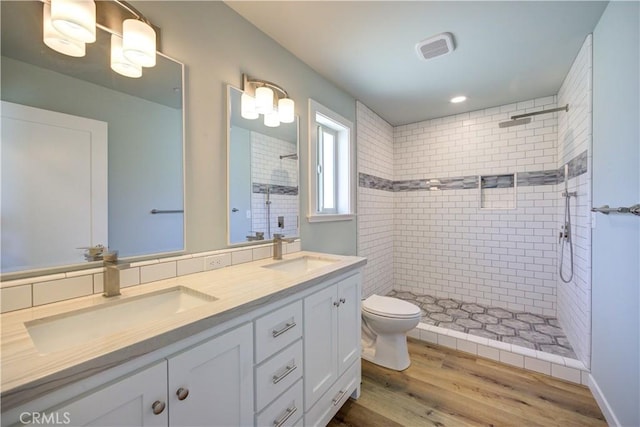 bathroom featuring vanity, hardwood / wood-style floors, toilet, and tiled shower