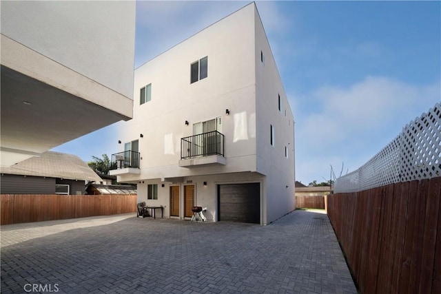 back of property with a garage, driveway, fence, and stucco siding