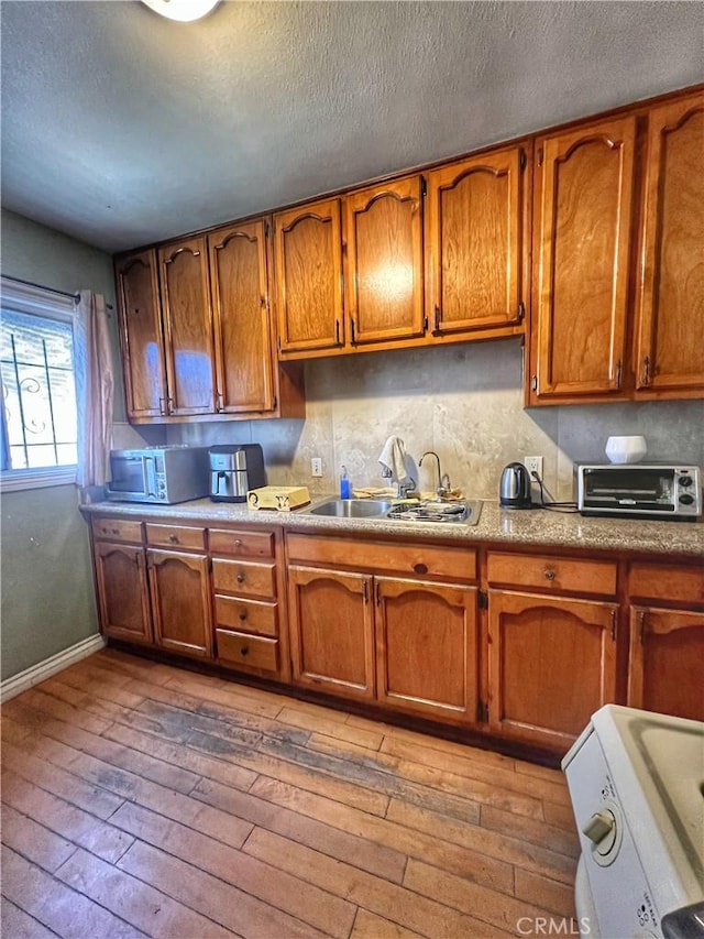 kitchen with a toaster, brown cabinets, light countertops, a sink, and wood finished floors