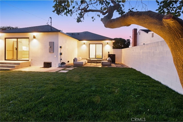 back house at dusk with a yard and a patio