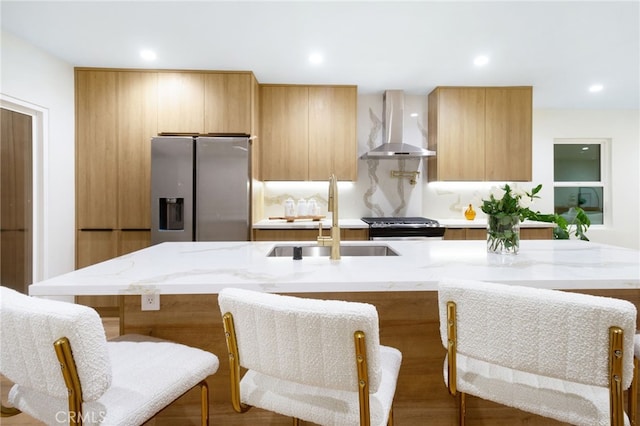 kitchen with appliances with stainless steel finishes, wall chimney exhaust hood, sink, and a breakfast bar area