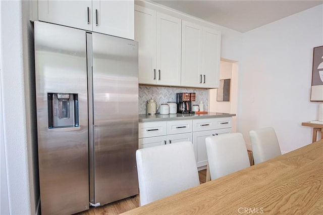 kitchen featuring stainless steel refrigerator with ice dispenser, white cabinetry, and backsplash