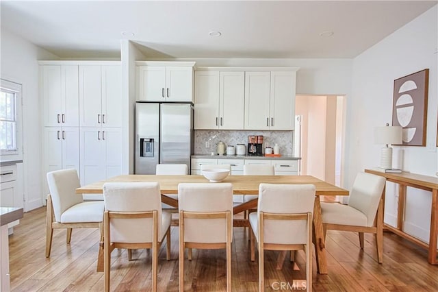 kitchen with white cabinetry, light wood-type flooring, stainless steel fridge with ice dispenser, and backsplash