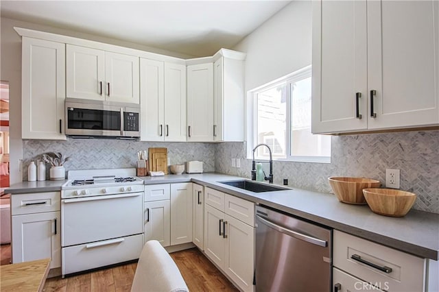 kitchen featuring sink, appliances with stainless steel finishes, white cabinetry, wood-type flooring, and decorative backsplash