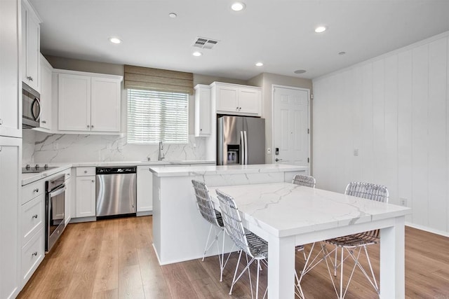 kitchen with a center island, a breakfast bar, visible vents, appliances with stainless steel finishes, and white cabinets