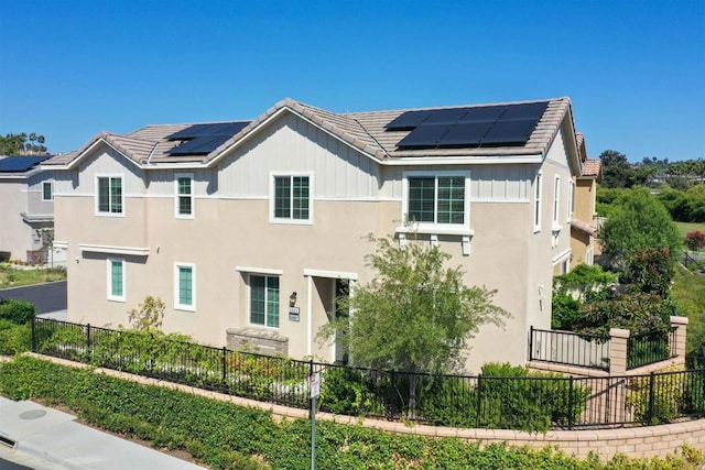 exterior space with a tile roof, stucco siding, board and batten siding, roof mounted solar panels, and fence private yard