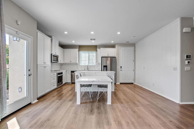 kitchen with light wood-style flooring, appliances with stainless steel finishes, white cabinetry, a kitchen island, and a kitchen bar