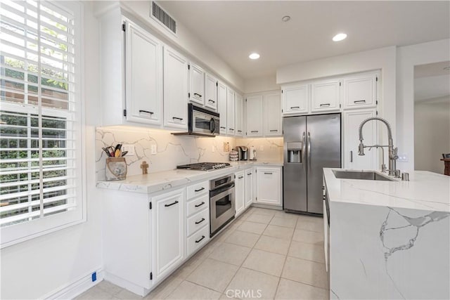 kitchen with sink, tasteful backsplash, stainless steel appliances, light stone countertops, and white cabinets