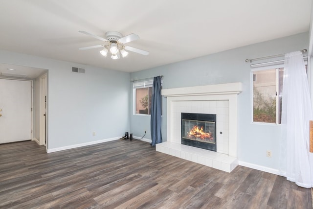 unfurnished living room with a tiled fireplace, a ceiling fan, dark wood-style floors, and visible vents