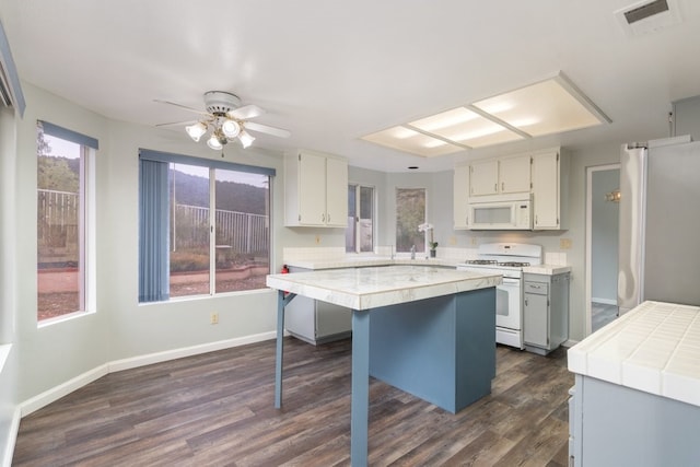 kitchen featuring a kitchen breakfast bar, a center island, ceiling fan, dark wood-type flooring, and white appliances