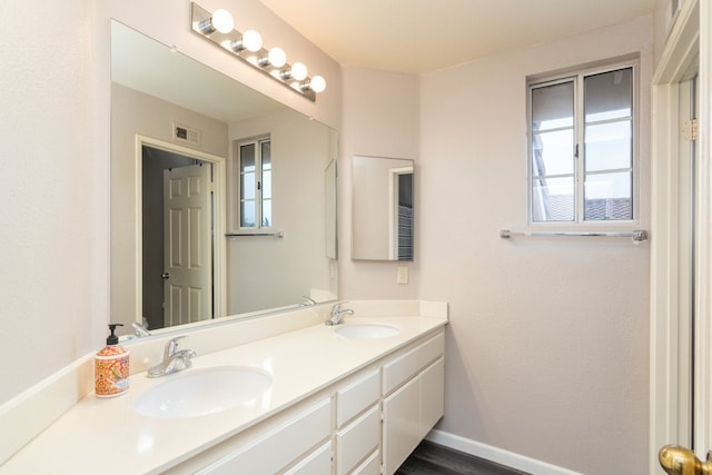 bathroom with a sink, baseboards, double vanity, and visible vents