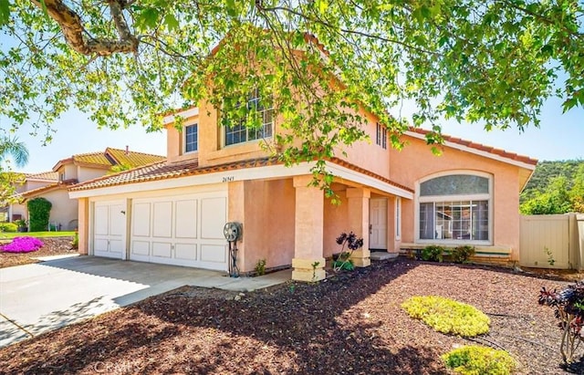 mediterranean / spanish house featuring a tiled roof, driveway, fence, an attached garage, and stucco siding